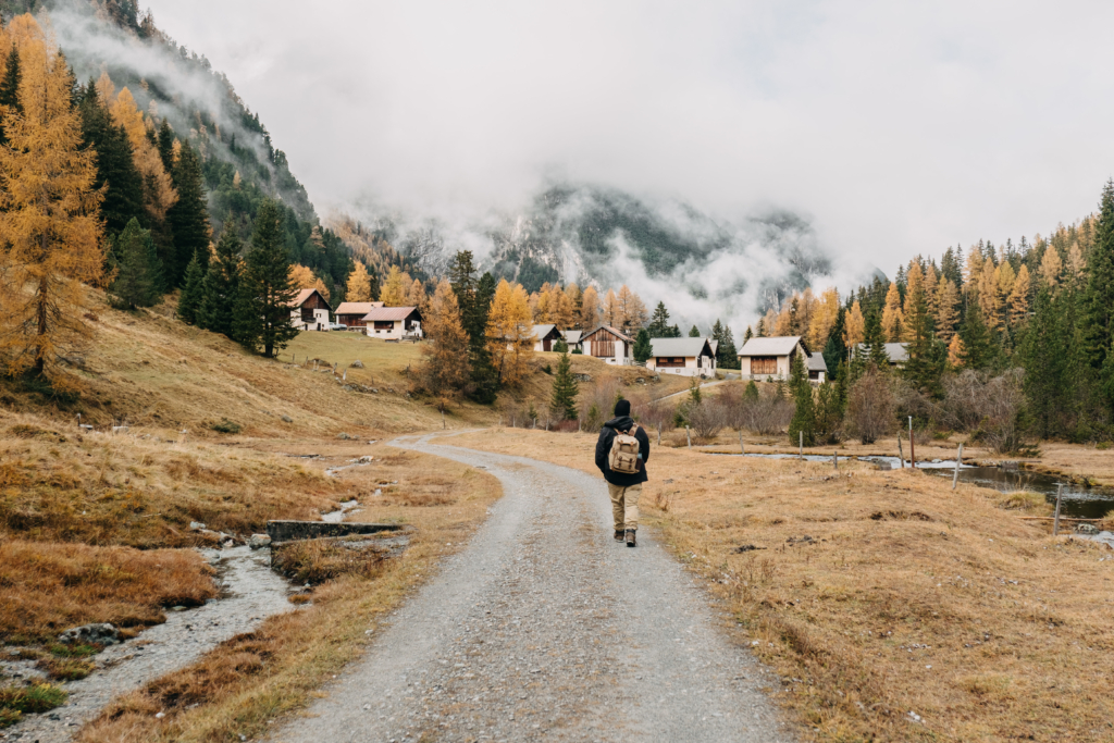 back view man hiker with backpack walking along footpath surrounded by autumn nature scenes
